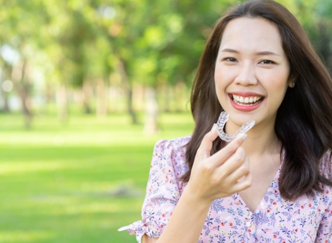 Smiling woman putting ClearCorrect clear aligner in her mouth outdoors