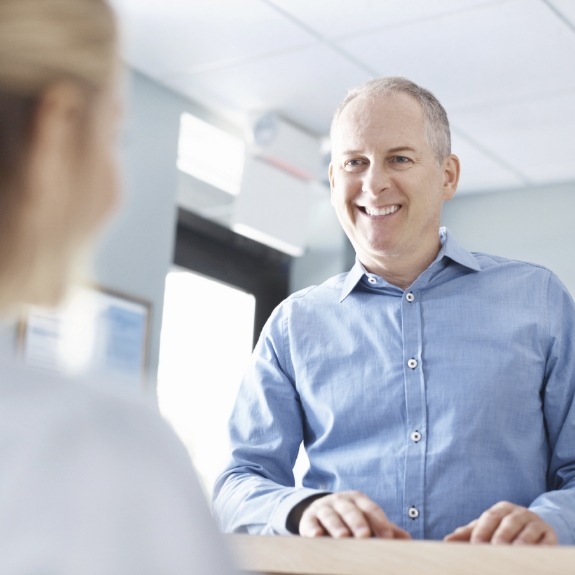Man smiling while talking to front desk dental team member