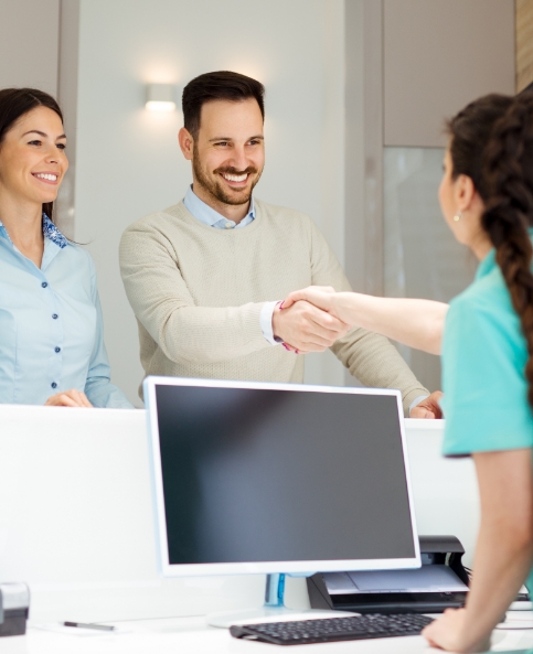 Dental team member at front desk shaking hands with dental patient